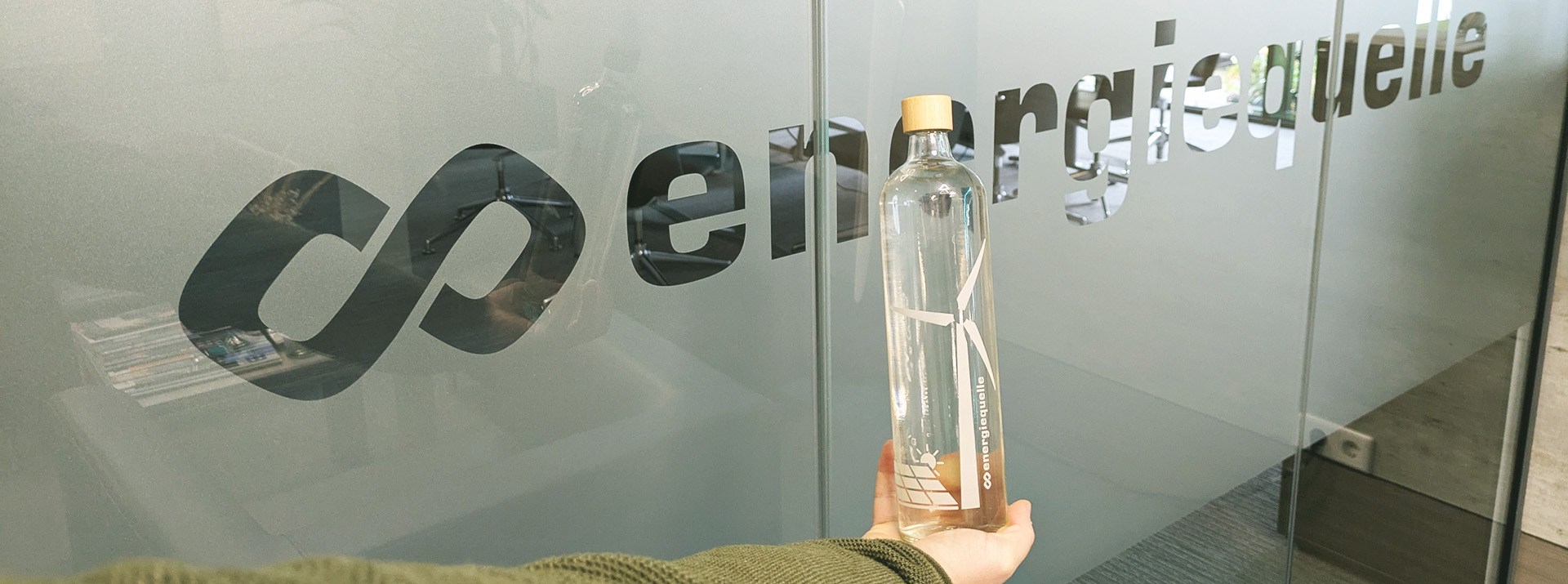 Ein Mitarbeiter hält eine bedruckte Glasflasche vor das Logo der Energiequelle GmbH