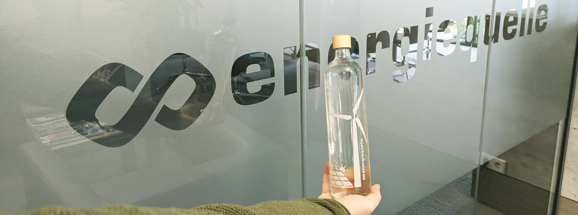 Mitarbeiter hält bedruckte Flasche in der Hand vor dem Logo der Energiequelle