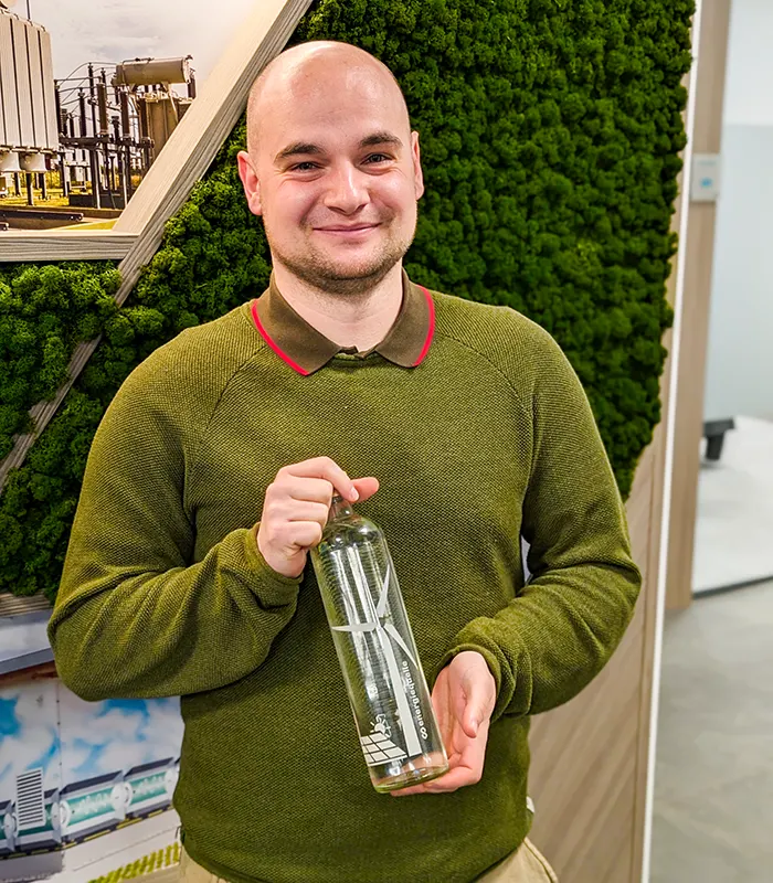 Fröhlicher Mitarbeiter der Energiequelle GmbH hält stolz eine Glasflasche mit Branding