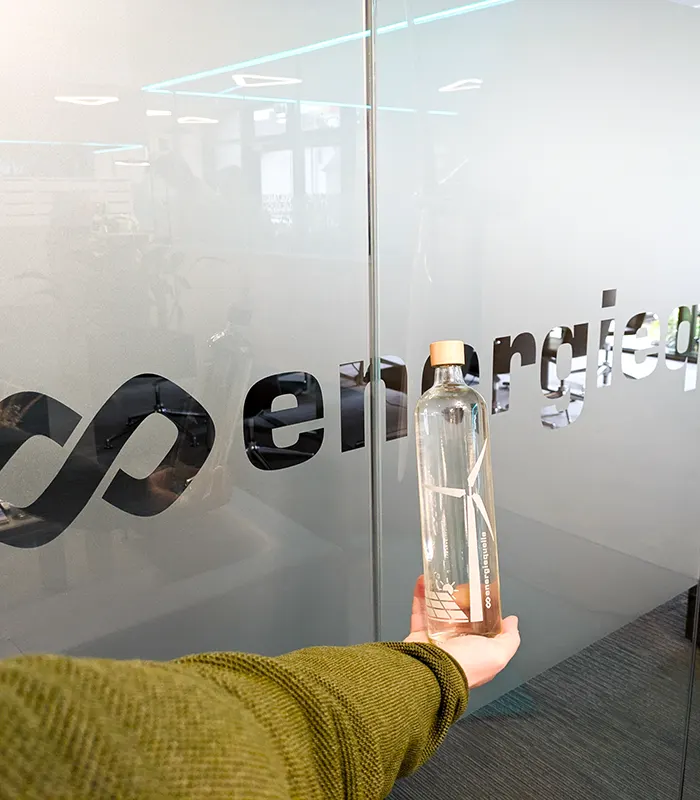 Mitarbeiter hält bedruckte Flasche in der Hand vor dem Logo der Energiequelle