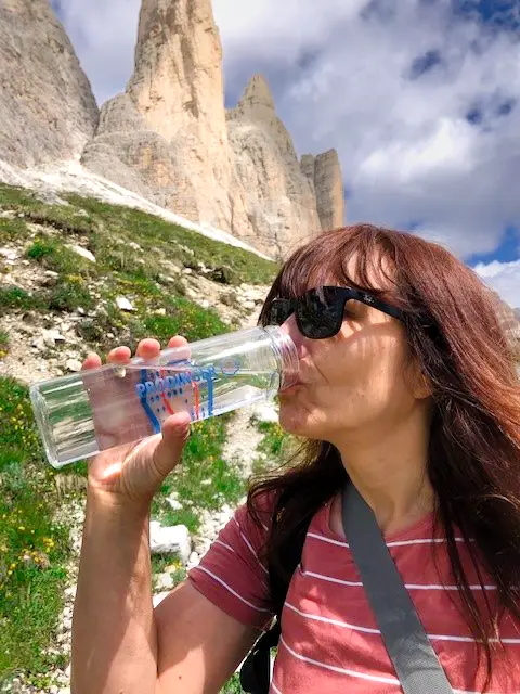 Mitarbeiterin von Prodinger trinkt Wasser aus einer bedruckten Flaschen bei einer Wanderung in den Dolomiten