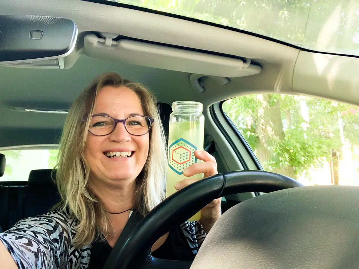Außendienstmitarbeiterin von Prodinger hält im Auto sitzend die bedruckte Flasche in die Kamera