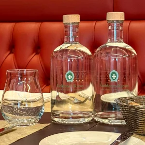 Bedruckte Wasserflaschen aus Glas auf einem gedeckten Tisch in einem Gasthaus