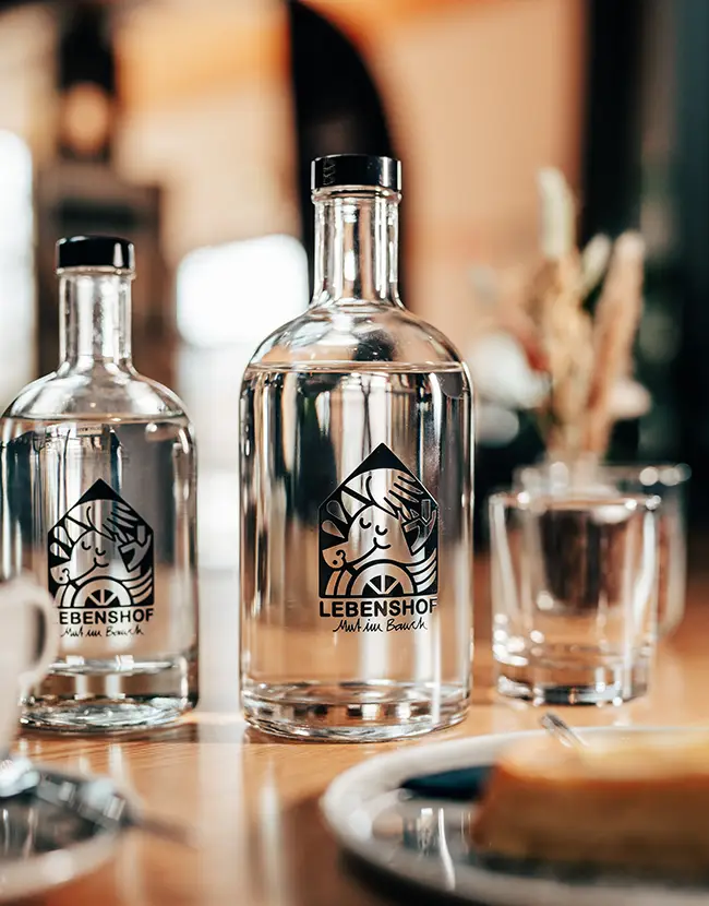 mit Logo bedruckte Flaschen auf einem gedeckten Tisch mit Kaffee und Kuchen